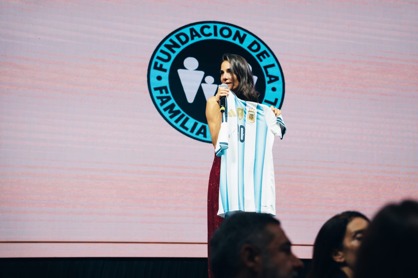 La conductora Juana Viale sostiene la camiseta de la selección argentina de fútbol en el escenario durante un acto de la Fundación de la Policía.