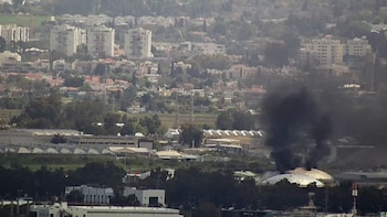 Vista aérea de una refinería de petróleo en Israel con una estructura abovedada de la que sale una gran columna de humo negro, con edificios residenciales al fondo