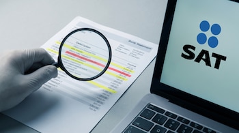 Una mano enguantada sostiene una lupa sobre un extracto bancario impreso con movimientos resaltados en amarillo y rojo. A un lado, una laptop muestra el logo del SAT.