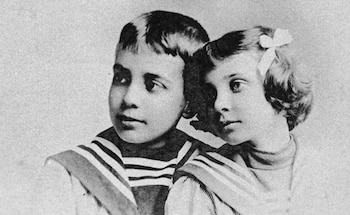 Una fotografía en blanco y negro muestra a un niño y una niña, ambos vestidos con atuendos de estilo marinero vintage, mirando al lado
