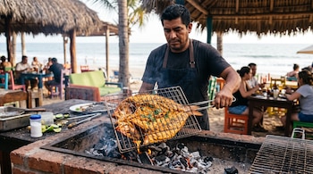 Hombre con delantal sostiene una parrilla metálica doble con un pescado entero abierto sobre brasas encendidas en un asador de ladrillos.