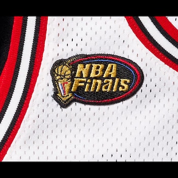 Primer plano del parche de las Finales NBA en una camiseta blanca perforada con detalles de franjas rojas, blancas y negras