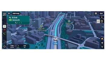 Captura de pantalla de Google Maps en vista 3D con un coche blanco en una autopista, ruta azul, edificios grises, indicaciones de giro y parques