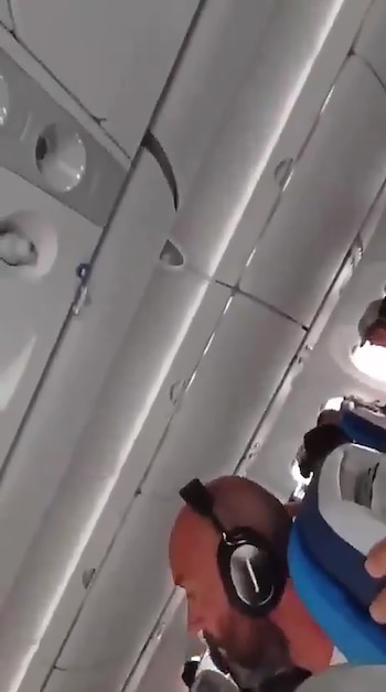 Vista en ángulo de la cabina de un avión con un hombre calvo usando auriculares en primer plano, el techo y paneles interiores blancos