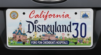 Placa vehicular de California blanca con la palabra "Disneyland" en grande, un castillo rosa, personajes animados y texto "FOR CHILDREN'S HOSPITALS" para niños.