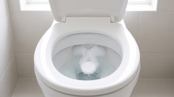 Un inodoro blanco de porcelana con la tapa abierta y una pastilla redonda que genera burbujas en el agua.