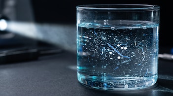 Vaso de vidrio con agua y partículas en suspensión iluminado por un haz de luz lateral sobre un fondo oscuro.