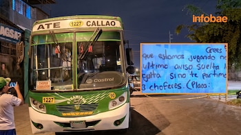 Bus verde y blanco de transporte público, con carteles "ATE" y "CALLAO", estacionado de noche. Una persona le toma una foto junto a una nota de amenaza visible