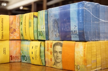 Primer plano de múltiples fajos de billetes de colones costarricenses, con denominaciones de 1000, 5000 y 10000, apilados sobre una superficie de madera.