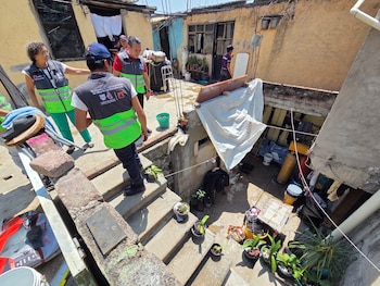 Varias personas con chalecos reflectantes bajan unas escaleras en un área residencial con edificios de poca altura y diversos objetos en el suelo