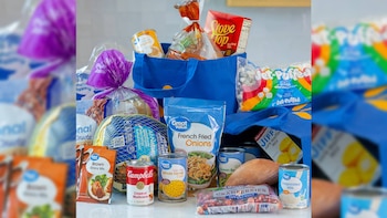 Bolsas de compras azules junto a un pavo congelado, latas de conservas, una batata, arándanos y paquetes de alimentos envasados