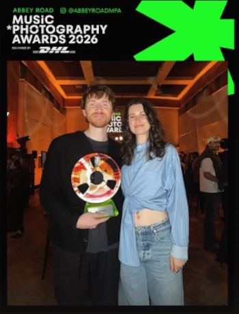 Un hombre sostiene un trofeo circular junto a una mujer frente a un panel de los Abbey Road Music Photography Awards