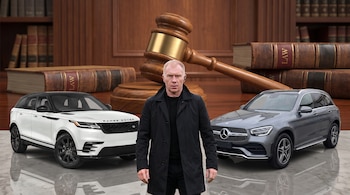 Un hombre de pie, un automóvil Range Rover blanco, un automóvil Mercedes gris, un mazo judicial, libros de derecho.
