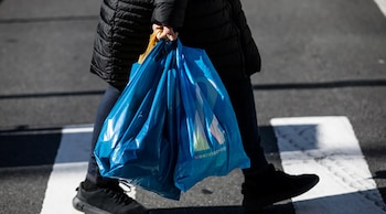 Primer plano de una persona llevando varias bolsas de plástico azules brillantes con un logo blanco, caminando sobre un paso de peatones rayado