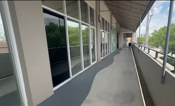 Un pasillo exterior cubierto de un edificio comercial con una fila de locales con grandes ventanales de vidrio y una barandilla al lado derecho