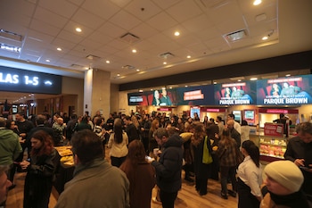 Un vestíbulo de cine abarrotado de gente, con pantallas digitales de Cinemark, un cartel de Salas 1-5, estaciones de comida y un techo con luminarias