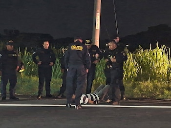 Agentes policiales uniformados permanecen junto a un hombre tendido en el asfalto durante la noche en una zona con vegetación