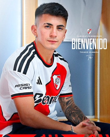 Primer plano de un hombre joven sentado con camiseta de fútbol blanca, roja y negra de River Plate, con escudo y patrocinadores