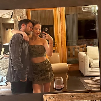 Selfie de Darío Cvitanich e Ivana Figueiras en un espejo; él la abraza por detrás mientras ella sostiene un teléfono. Un vaso de vino tinto en primer plano