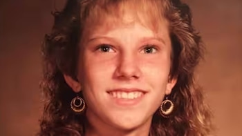 Fotografía de una joven de cabello ondulado con flequillo y pendientes circulares que sonríe ante un fondo marrón