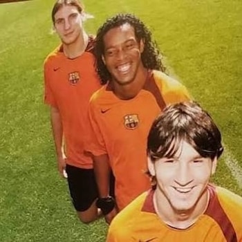 Tres futbolistas vestidos con camisetas de color naranja del FC Barcelona posan sonrientes sobre el césped de un campo de fútbol