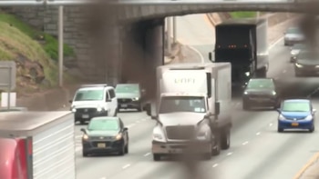 Un camión blanco con el logo 'UNFI' en el remolque avanza por una autopista con otros camiones, furgonetas y coches, bajo un puente