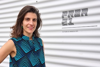 Lucie Haguenauer sonríe a cámara. Viste blusa sin mangas azul y negra. Al fondo, pared blanca con logo y dirección Av. Pedro de Mendoza 2073