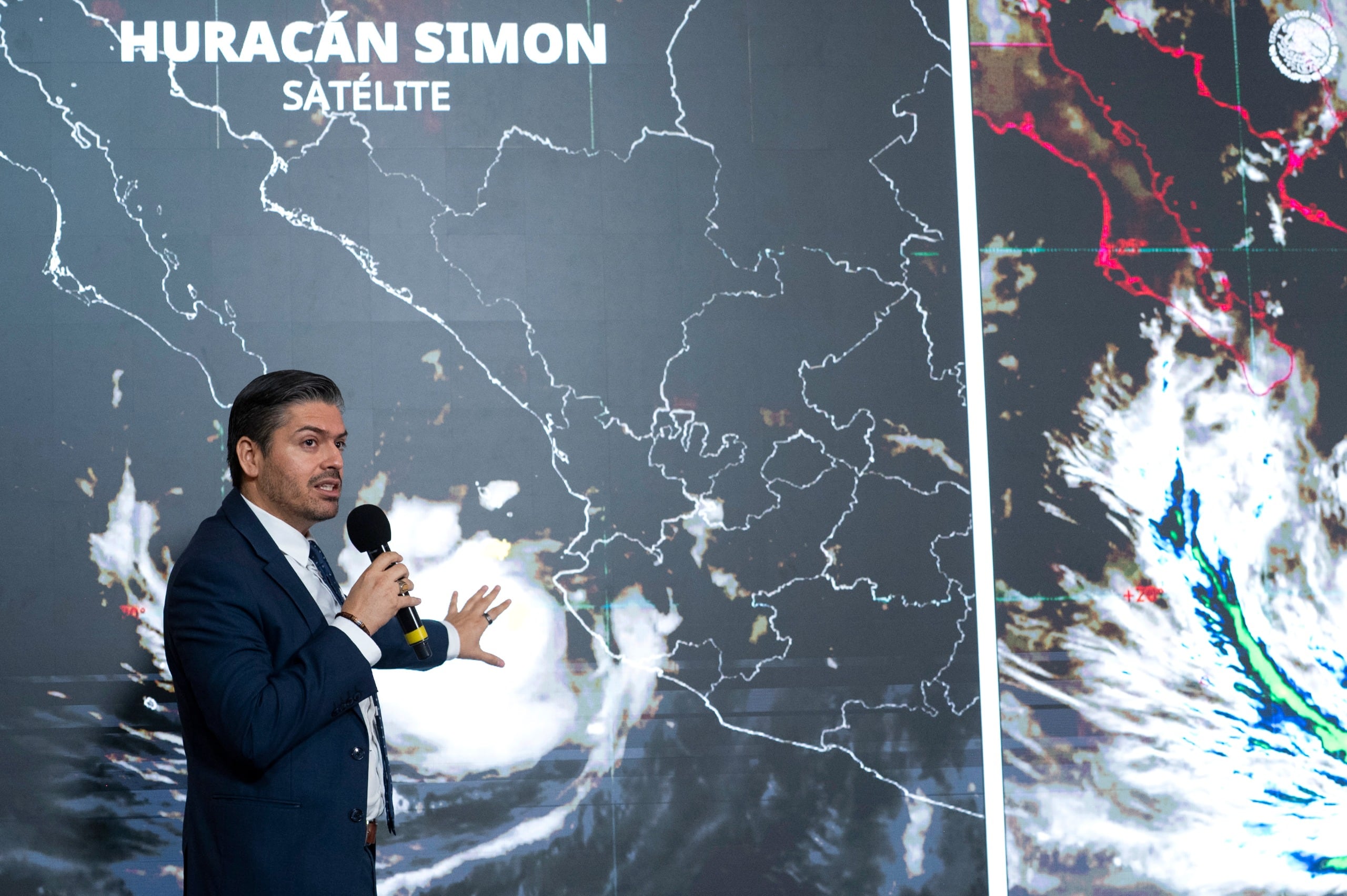 Un funcionario expone datos sobre la trayectoria del huracán Simon frente a un mapa satelital de México.