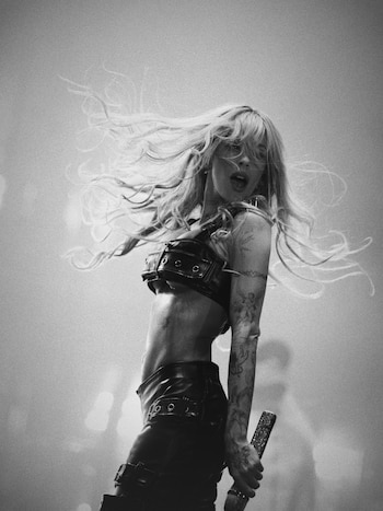 Fotografía en blanco y negro de Tini Stoessel sobre un escenario con el cabello al aire y un micrófono en la mano