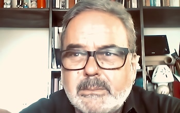Un hombre de cabello canoso y anteojos mira hacia un costado frente a una biblioteca