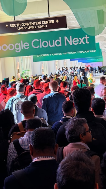Uma grande multidão vista de trás enche o corredor interno. Placas para 'Google Cloud Next' e 'SOUTH CONVENTION CENTER'