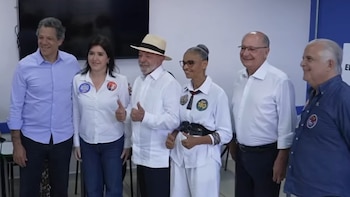 Seis personas posan sonriendo en una sala blanca, entre las cuales un hombre viste sombrero de paja y camisa blanca