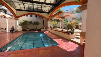 Patio interior con piscina cubierta por un techo de cristal, arcos de color naranja y blanco, plantas y un cartel de Baja del Sol