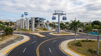 Vista aérea de una intersección vial moderna en Los Alcarrizos con asfalto nuevo, señalización, teleférico de Santo Domingo y señales del Metro, bajo cielo nublado.
