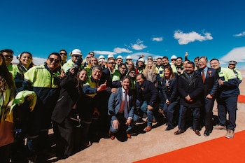 Un grupo de personas con trajes formales y chaquetas de alta visibilidad posa para una fotografía al aire libre bajo un cielo despejado