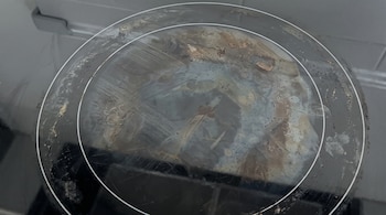 Quemador circular de una placa vitrocerámica negra con manchas marrones de grasa seca y marcas sobre el vidrio.