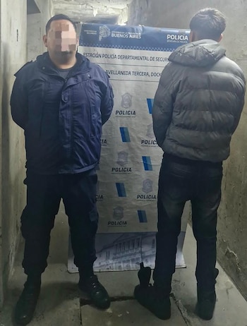 Un agente policial junto a un hombre detenido de espaldas ante un cartel de la Policía de la Provincia de Buenos Aires
