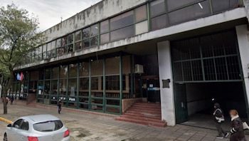 Exterior del Ministerio de Salud de Entre Ríos, un edificio de dos pisos con amplias ventanas, escaleras de ladrillo y un gran portón, con un coche plateado y peatones en la acera