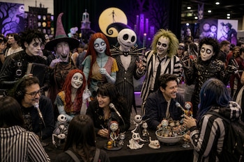 Varias personas caracterizadas con disfraces y maquillaje posan detrás de una mesa con pequeñas figuras y micrófonos.