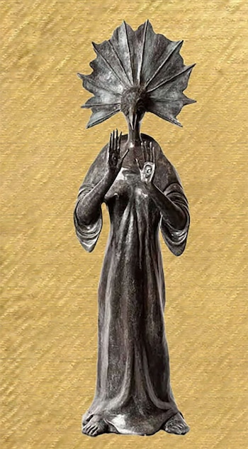 Escultura de bronce de una figura antropomórfica oscura con un tocado en forma de abanico, túnica fluida y manos levantadas, sobre un fondo amarillo texturizado