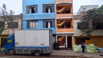 Un camión azul estacionado frente a un edificio colorido, dos policías junto a la entrada y paquetes apilados en la acera