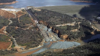 Vista aérea de un canal de concreto roto en una colina, con desprendimiento de rocas y tierra hacia un curso de agua junto a un embalse