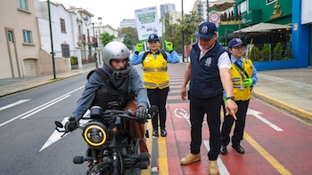 Un motociclista junto a tres fiscalizadores municipales, uno de los cuales sostiene un cartel sobre fiscalización electrónica vehicular