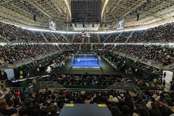 Vista aérea de un estadio cubierto lleno de gente, observando una cancha de pádel azul donde dos parejas de jugadores disputan un partido