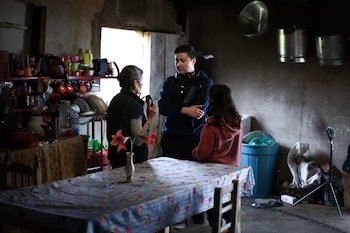 Un técnico sostiene un difusor junto a una cámara de cine, un micrófono de caña y dos personas frente a una cerca en el campo