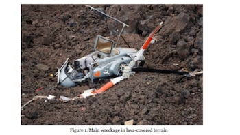 Un helicóptero gris destrozado yace sobre un suelo marrón oscuro y rocoso, con el fuselaje y las palas del rotor rotas visibles