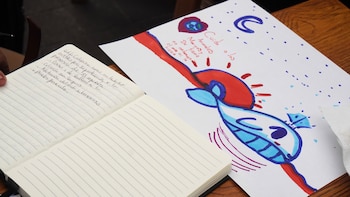 Primer plano de un dibujo infantil de una ballena y el planeta Tierra con el texto "Cuida a los Animales Marinos" junto a un cuaderno con notas