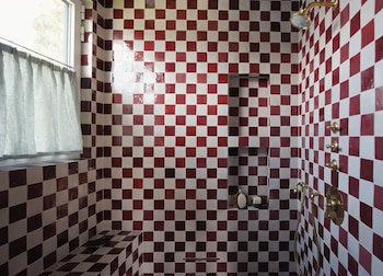 Ducha con paredes y banco cubiertos de azulejos Zellige cuadrados rojos y blancos en patrón de tablero de ajedrez, con una ventana y accesorios dorados
