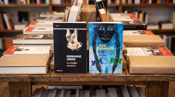 Dos libros de portada visible: "La mujer eunuco" y "Ojos azules". Se encuentran sobre una mesa de madera en una librería con más libros al fondo.