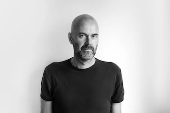 Retrato en blanco y negro de un hombre calvo con barba, vestido con una camiseta oscura, mirando directamente al frente contra un fondo blanco liso